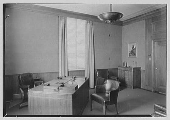 A 1941 private office: a desk, two leather armchairs, a tall curtained window, a cabinet, a framed picture and a door.